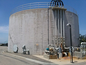 A large cylindrical storage tank with pipes and valves on the side, set against a clear blue sky.