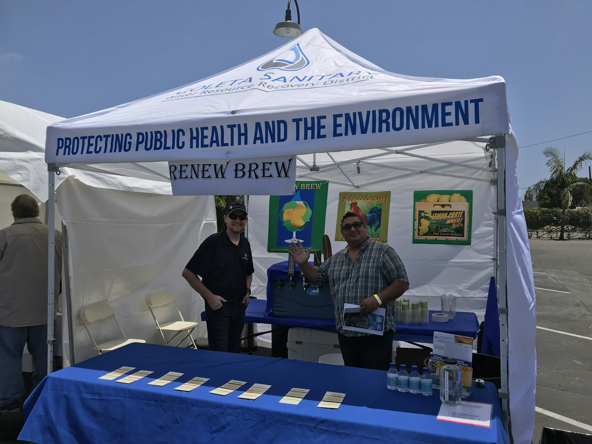 A booth promoting public health and environmental awareness, featuring two men, informational materials, and beverages.