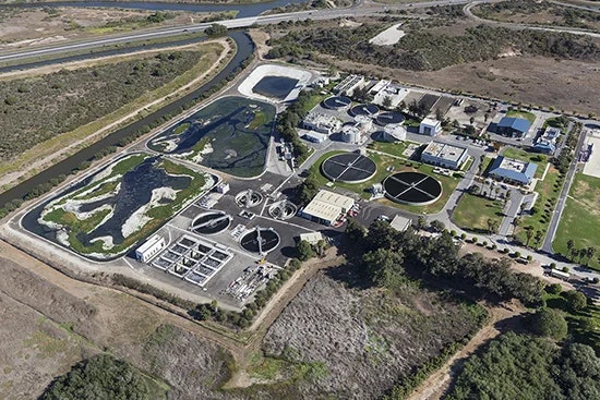 The image shows an aerial view of a wastewater treatment facility with various treatment ponds and processing buildings.