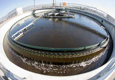 The image shows a circular water treatment facility with large tanks and a rotating mechanism for cleaning water.