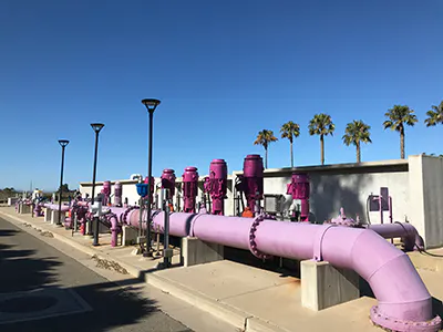 The image shows a row of large purple pipes and equipment, likely part of an industrial or water treatment facility, under a clear blue sky.