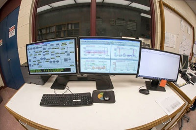 A desk with multiple computer monitors displaying technical data and graphs, along with a keyboard and mouse.
