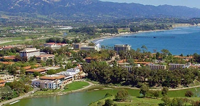 The image shows a coastal landscape with a town, buildings, a body of water, and mountains in the background.