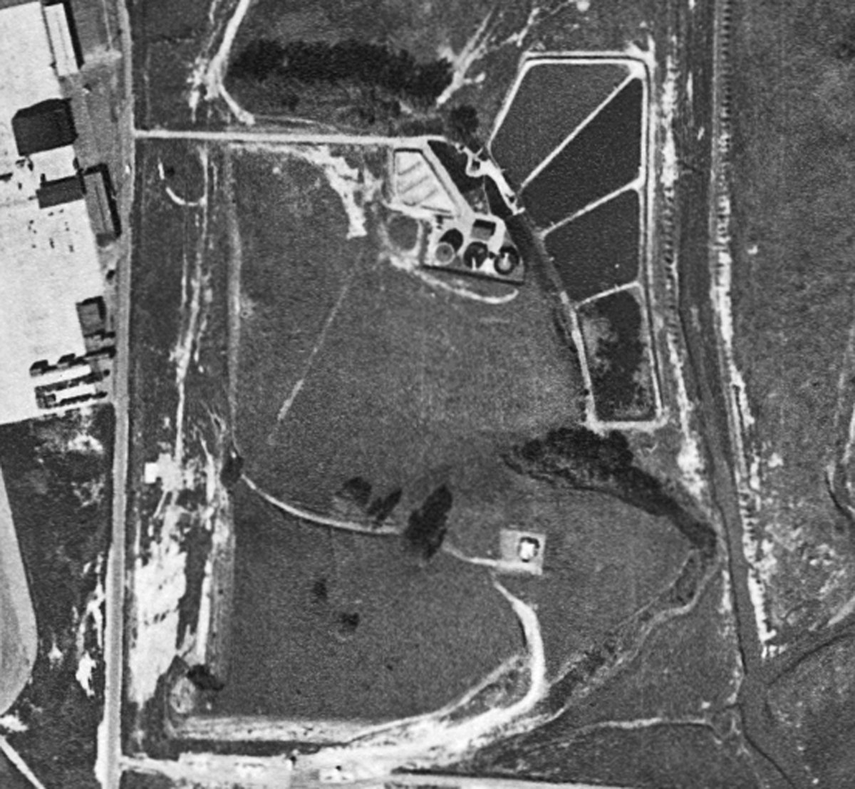 An aerial view of a facility with ponds, dirt paths, and nearby structures, likely related to industrial or agricultural use.