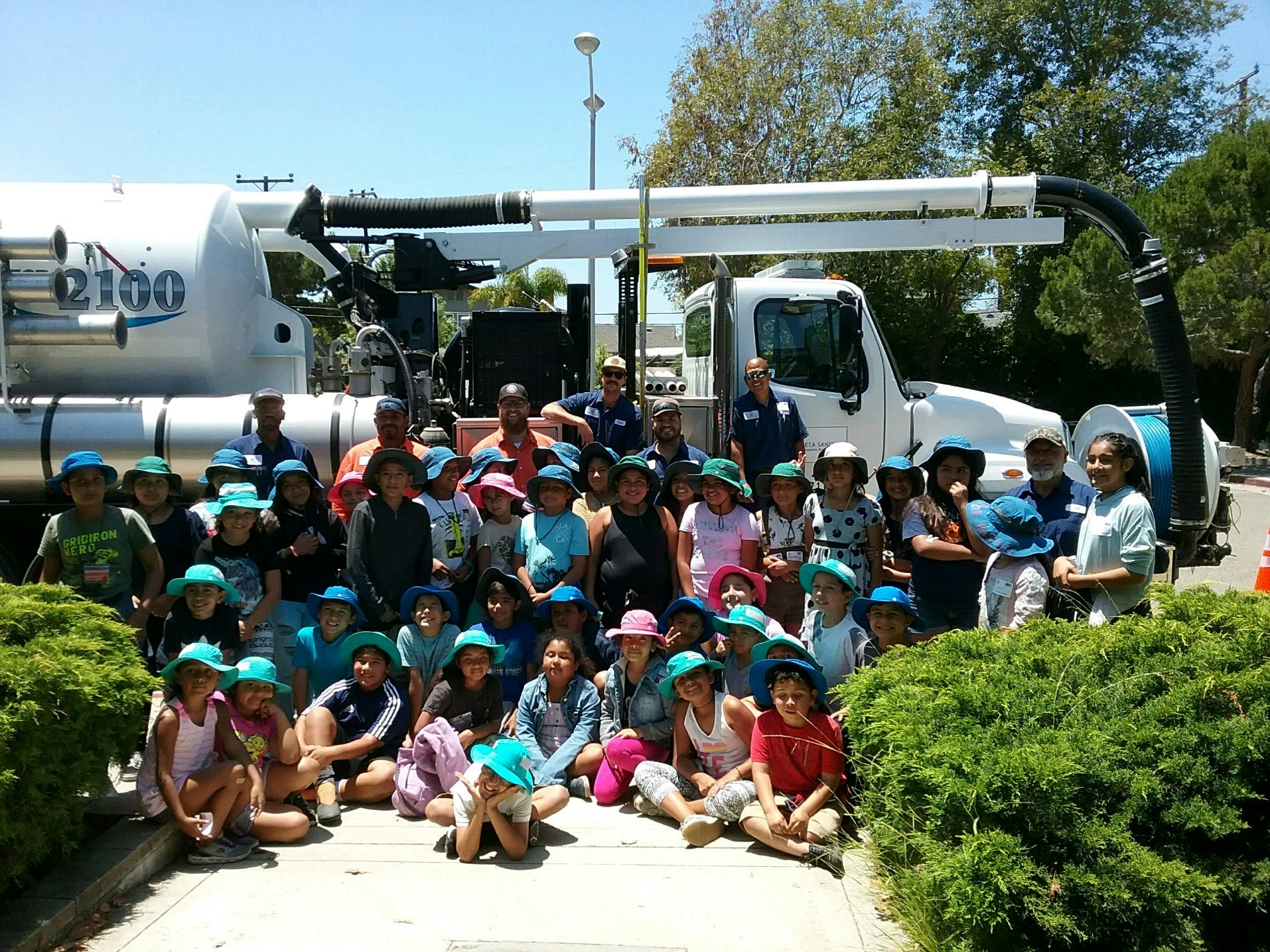 A large group of children wearing blue hats posing in front of a truck, likely during an educational or fun event.