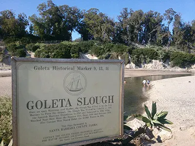 A historical marker for Goleta Slough, with a view of the slough and surrounding vegetation, indicating its significance in Santa Barbara County.