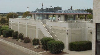 A modern building with a patio and stairs, surrounded by greenery and lamp posts, set in a scenic landscape.