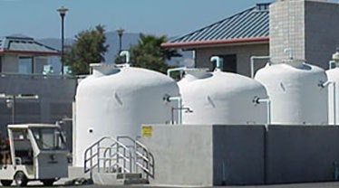 The image shows large white storage tanks near buildings and a small vehicle parked nearby.