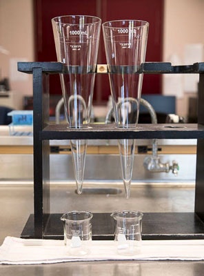 The image shows two large graduated cylinders and two smaller beakers on a lab stand, typical equipment for measuring liquids.