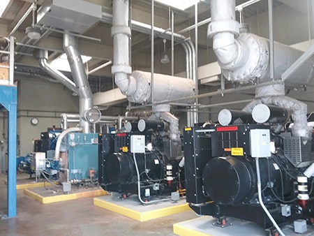 The image shows a mechanical room with several large industrial machines, pipes, and ventilation systems.