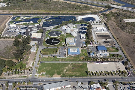 An aerial view of a water treatment facility featuring circular tanks, buildings, and landscaped areas.