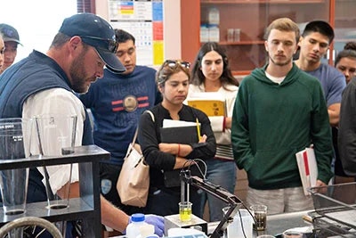 A teacher demonstrates a science experiment to a group of engaged students in a laboratory setting.