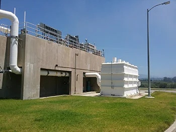 The image shows a large industrial facility with pipes, a storage tank, and a grassy area. The setting appears to be outdoors.