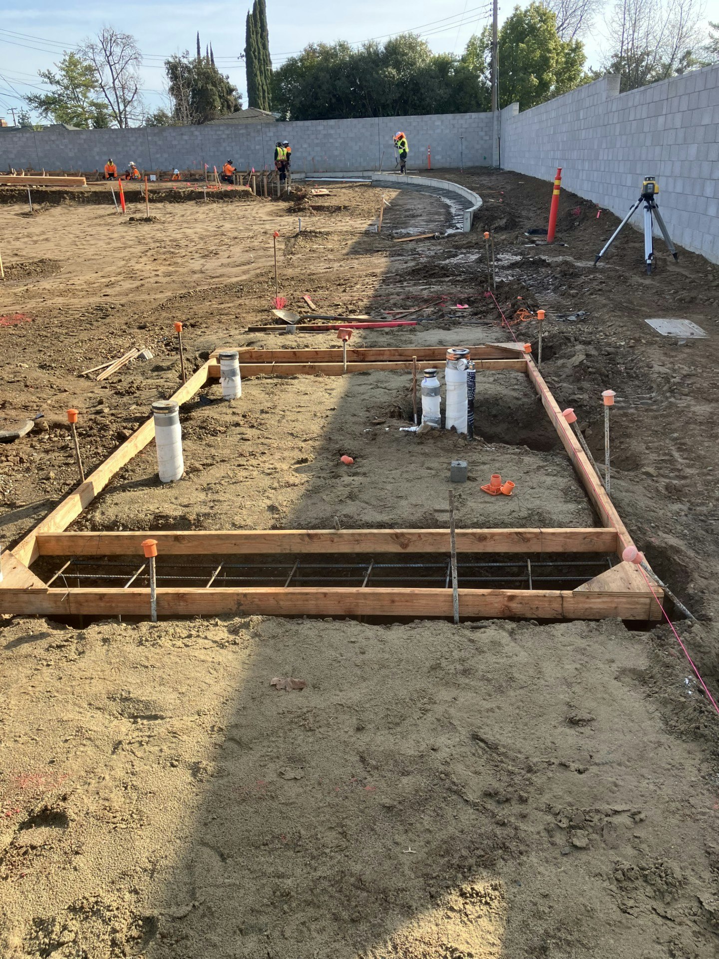 A construction site with foundation framing, workers in safety gear, and equipment for laying the groundwork is visible.