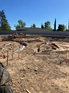 A construction site with excavated earth, framing, and workers preparing for building foundations under clear blue skies.
