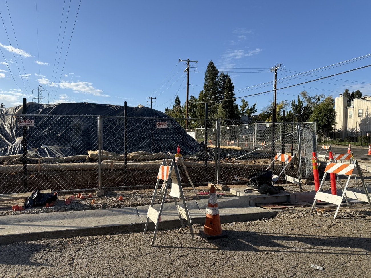 emPOWERment Park Construction site with fencing, caution signs, and traffic cones under a clear sky.