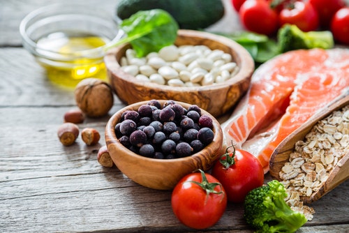 Assorted healthy foods: salmon, berries, beans, tomatoes, broccoli, nuts, oats, and olive oil.