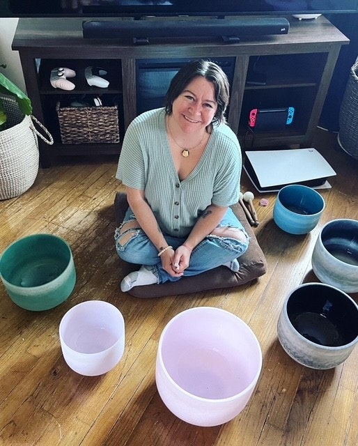 A person sitting on the floor surrounded by colorful bowls, with a TV stand and gaming controllers in the background.