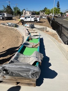 The image shows a construction site with a walkway under development, featuring green materials and construction equipment nearby.