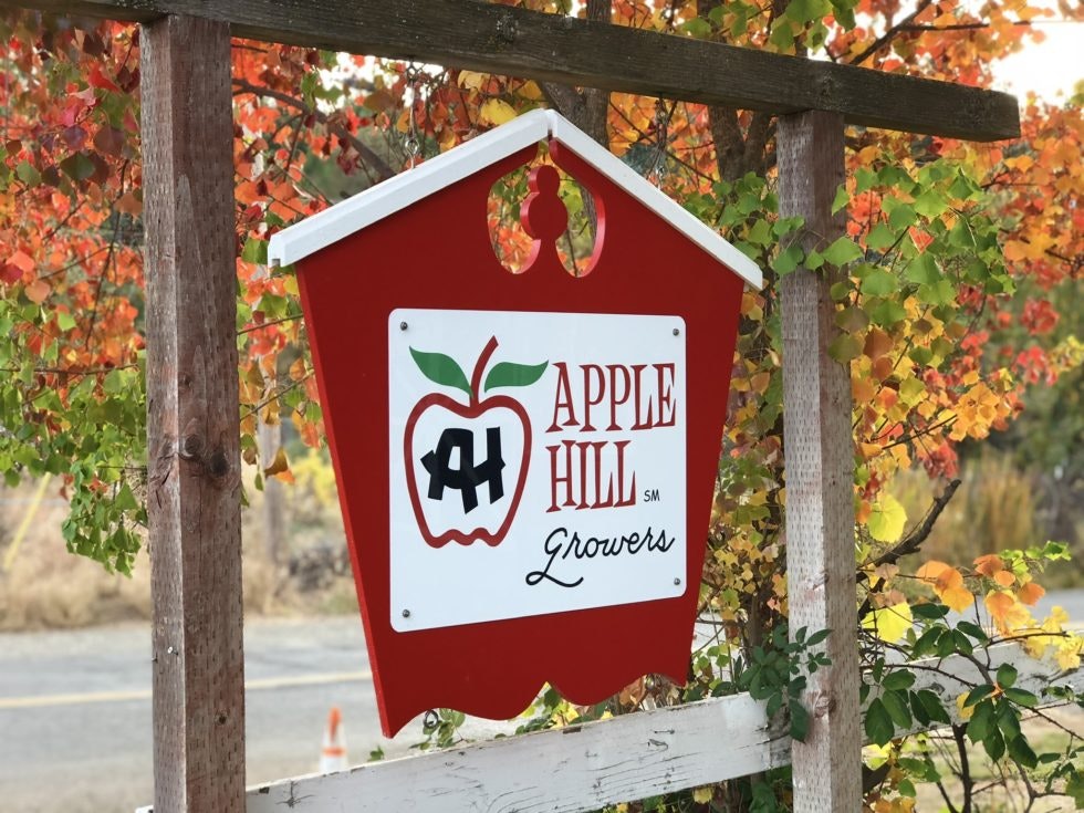 Sign for "Apple Hill Growers" with apple logo, surrounded by autumn-colored leaves.