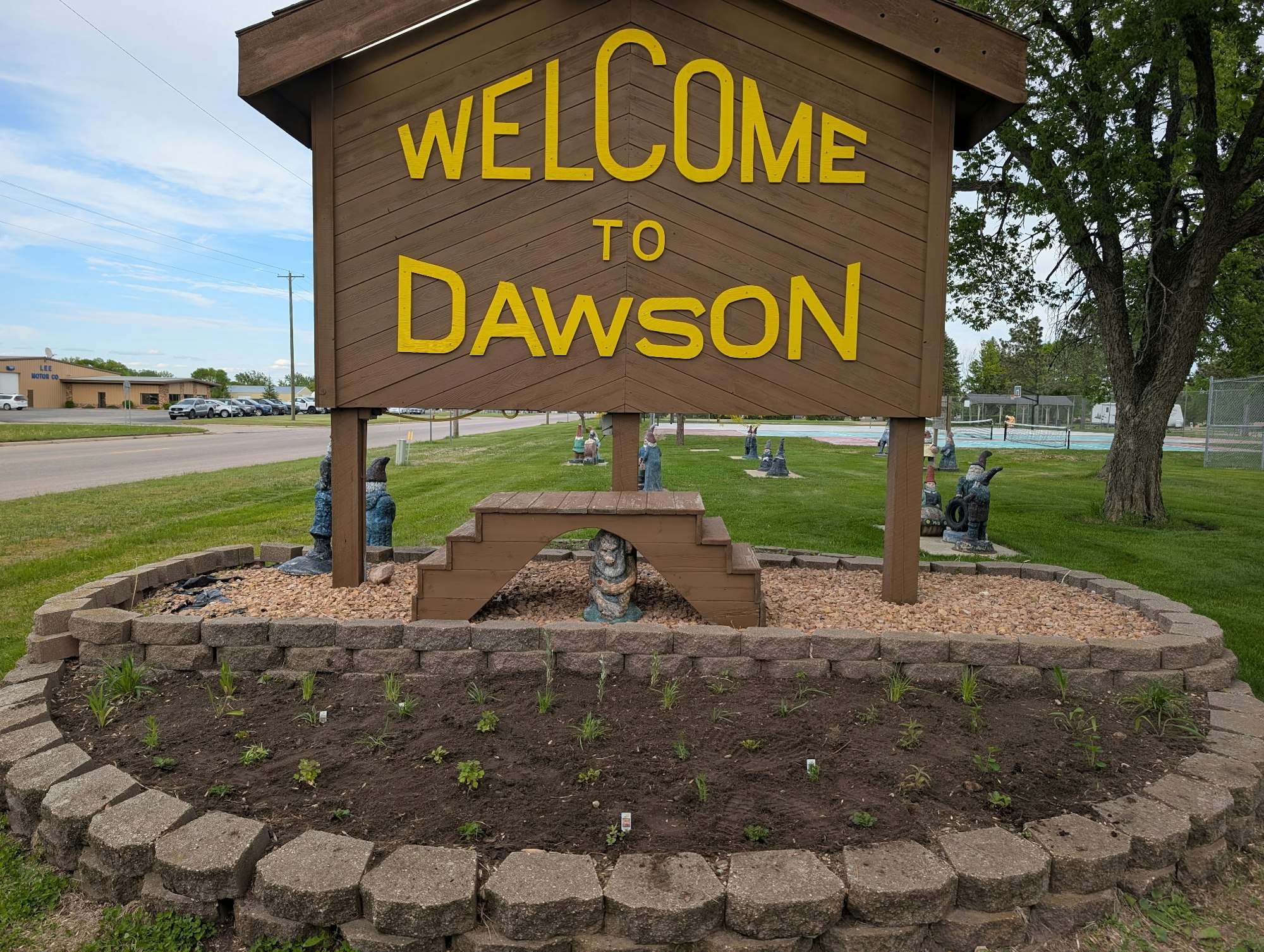 Sign reads "Welcome to Dawson" with garden and gnome statues underneath.