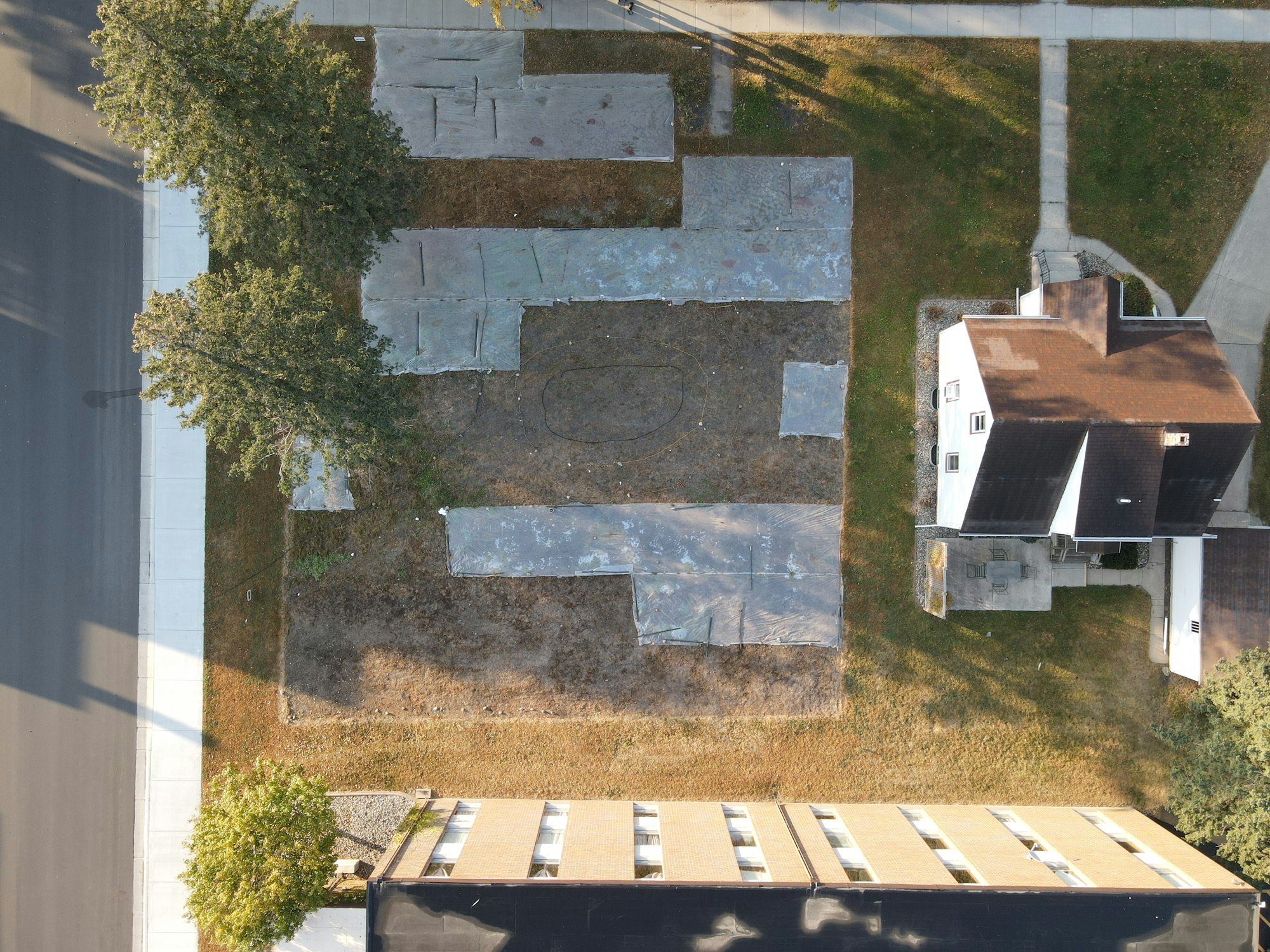 Aerial view of a house, neighboring buildings, trees, and a sidewalk along a street.