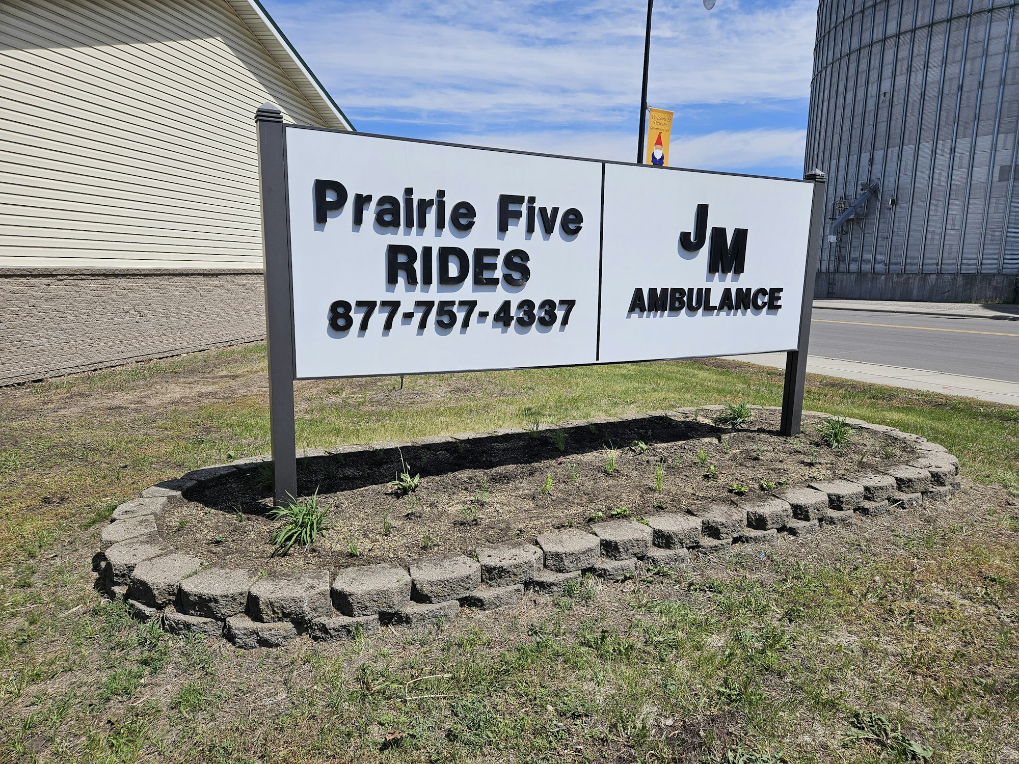 Sign for Prairie Five Rides and JM Ambulance with contact number, set in a small landscaped area.