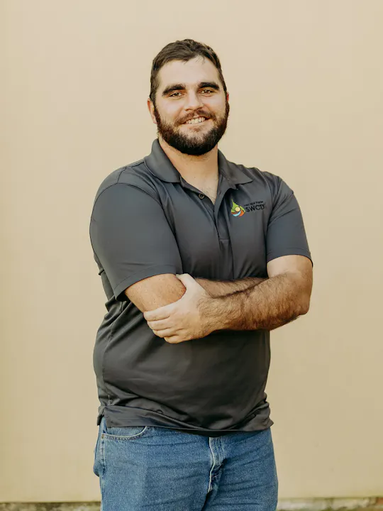 A man in a gray polo shirt stands smiling with arms crossed.
