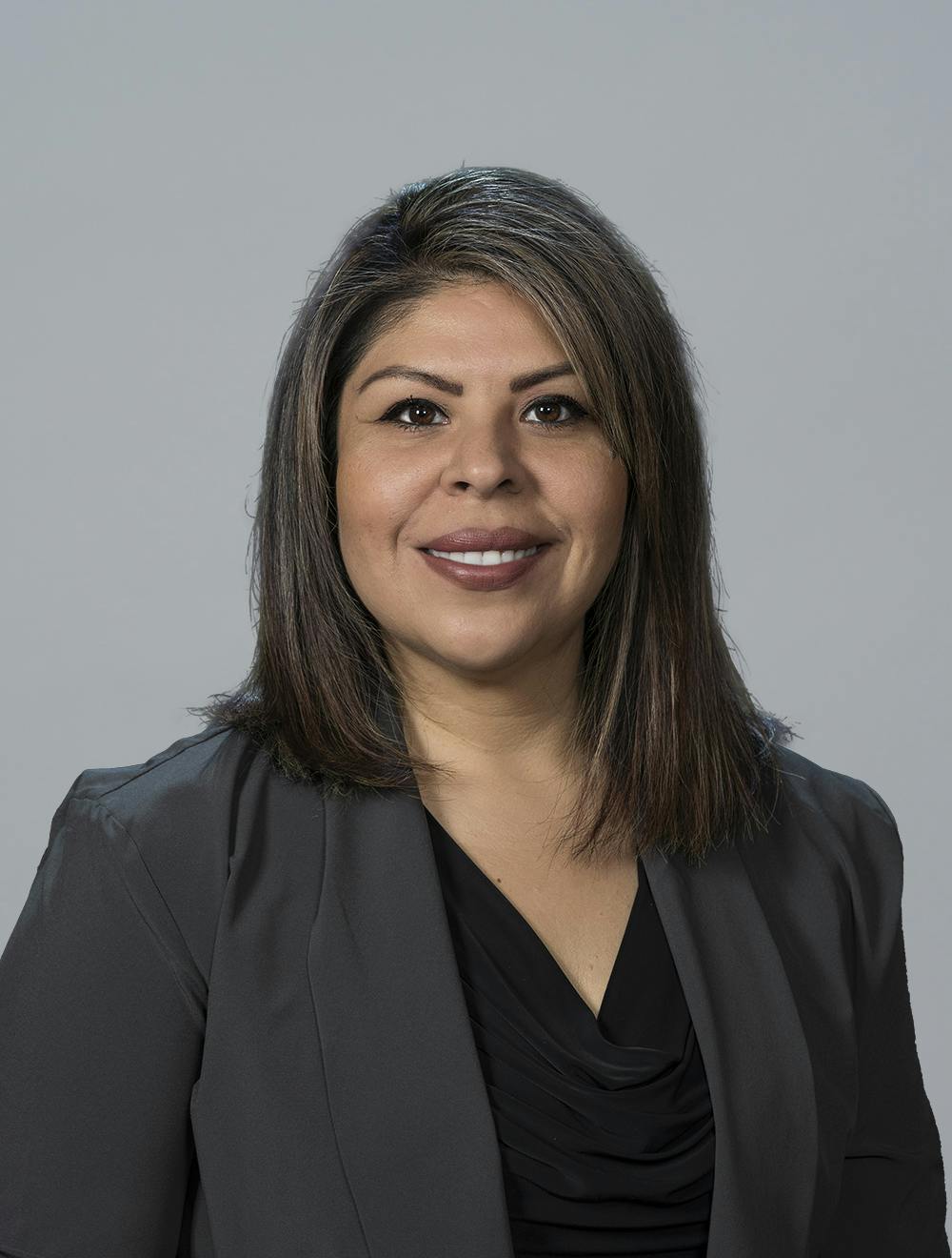 A woman in business attire smiling against a gray background.