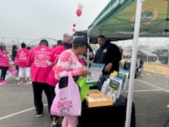 People in pink shirts at an outdoor event with a booth and balloons.