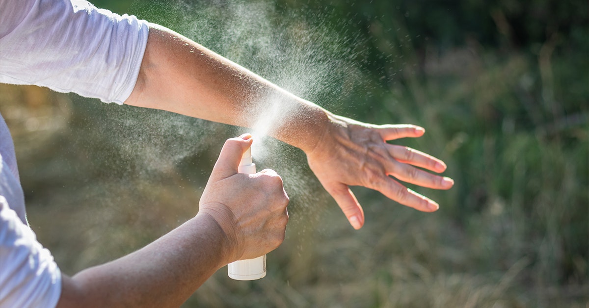 A person sprays a bottle of mist onto their forearm outdoors.