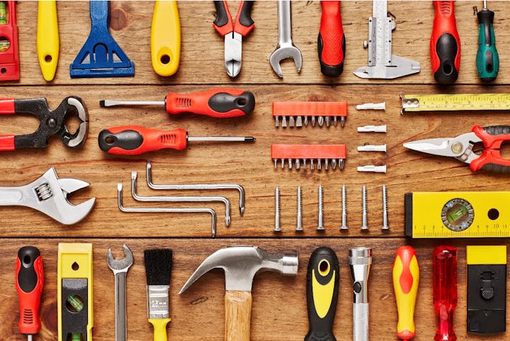 Assorted tools on a wooden surface, including screwdrivers, pliers, wrenches, screws, a hammer, and measuring tools.