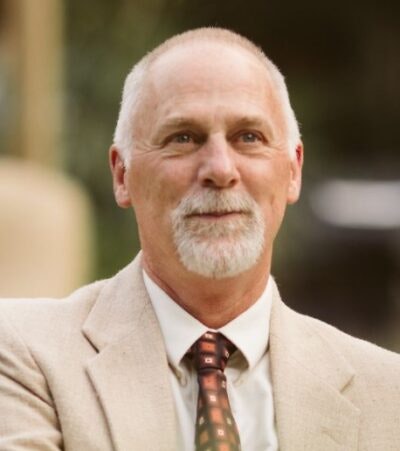 A man with a beard, wearing a suit and tie, is looking ahead.