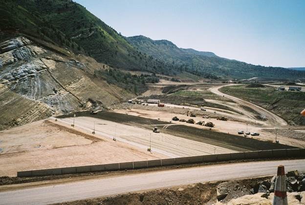 A construction site with heavy machinery and a road leading through hilly terrain.