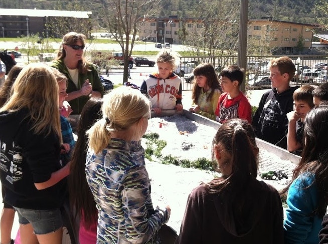 A group of students gather around for an educational outdoor activity, possibly a science demonstration or class.