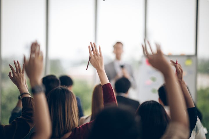 An audience with raised hands during a presentation or lecture.
