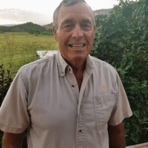A smiling man in a light shirt with natural scenery in the background.