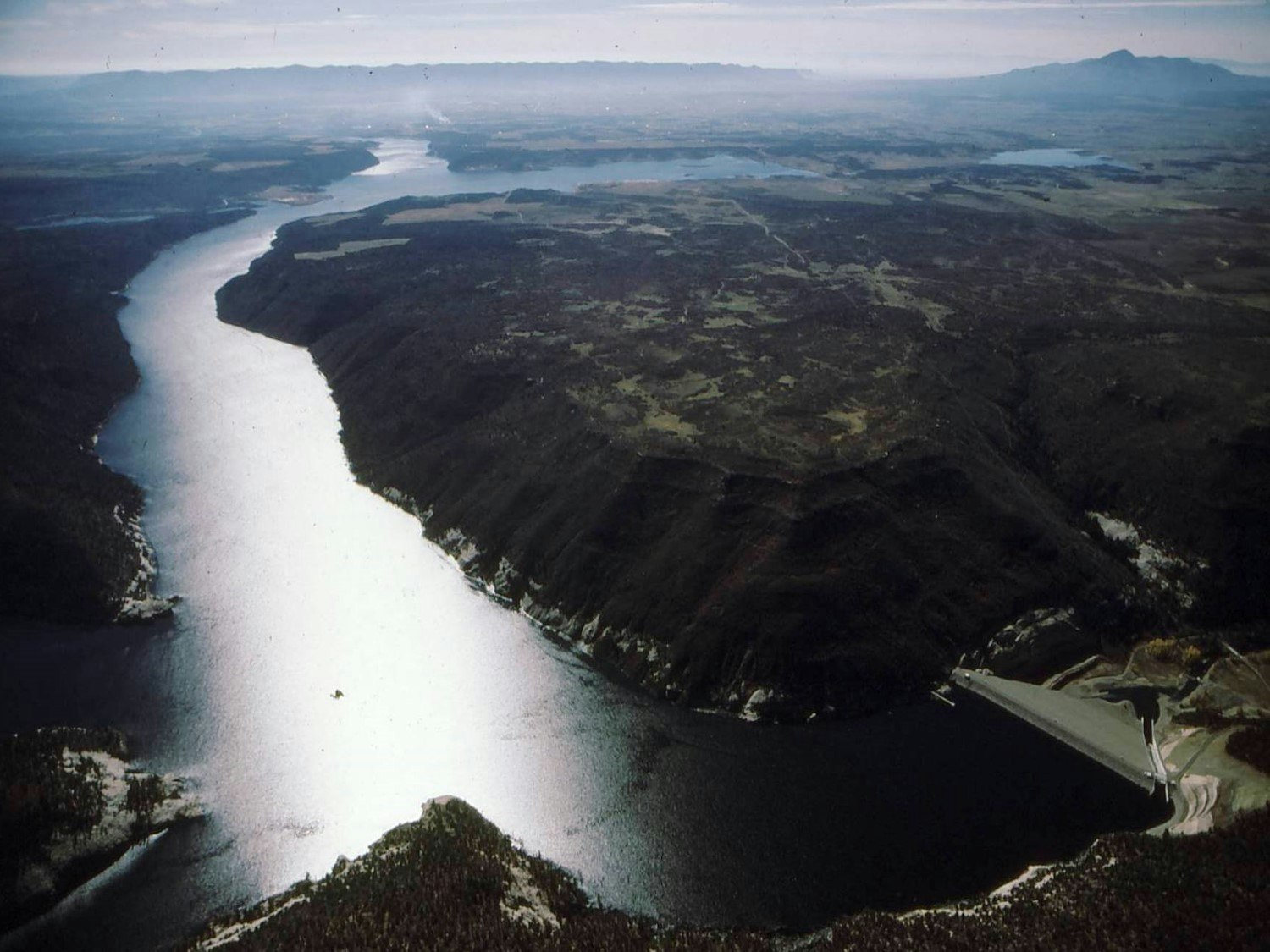 Aerial view of a dam with a reservoir stretching through hilly terrain.