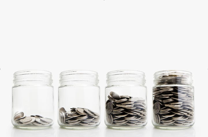 Four glass jars containing increasing amounts of coins, arranged in a row.