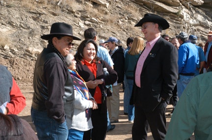 Group of people, some in cowboy hats, talking outdoors with rocky backdrop.