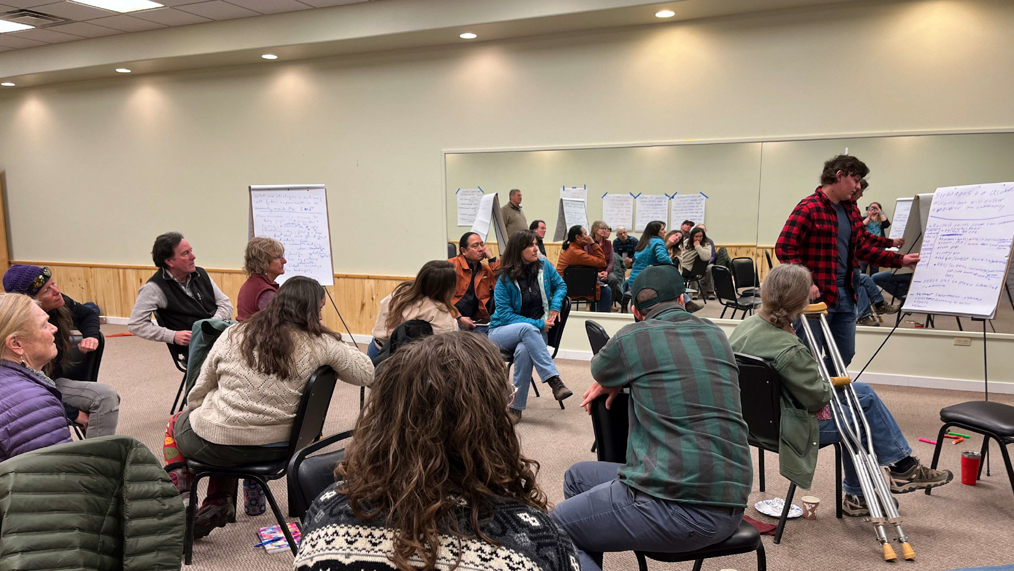 Group of people seated in a circle at a meeting with flip charts.