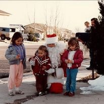 Three children with a Santa Claus figure on a residential street, light snow on the ground.