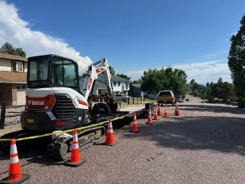 Construction equipment on a trailer with traffic cones nearby, parked on a street under a clear sky.