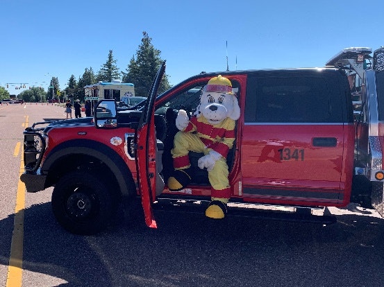 A person in a dog mascot costume sits in a red emergency vehicle parked on a road.
