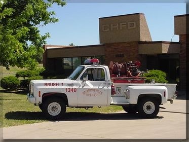 Vintage brush fire truck outside a fire department building.