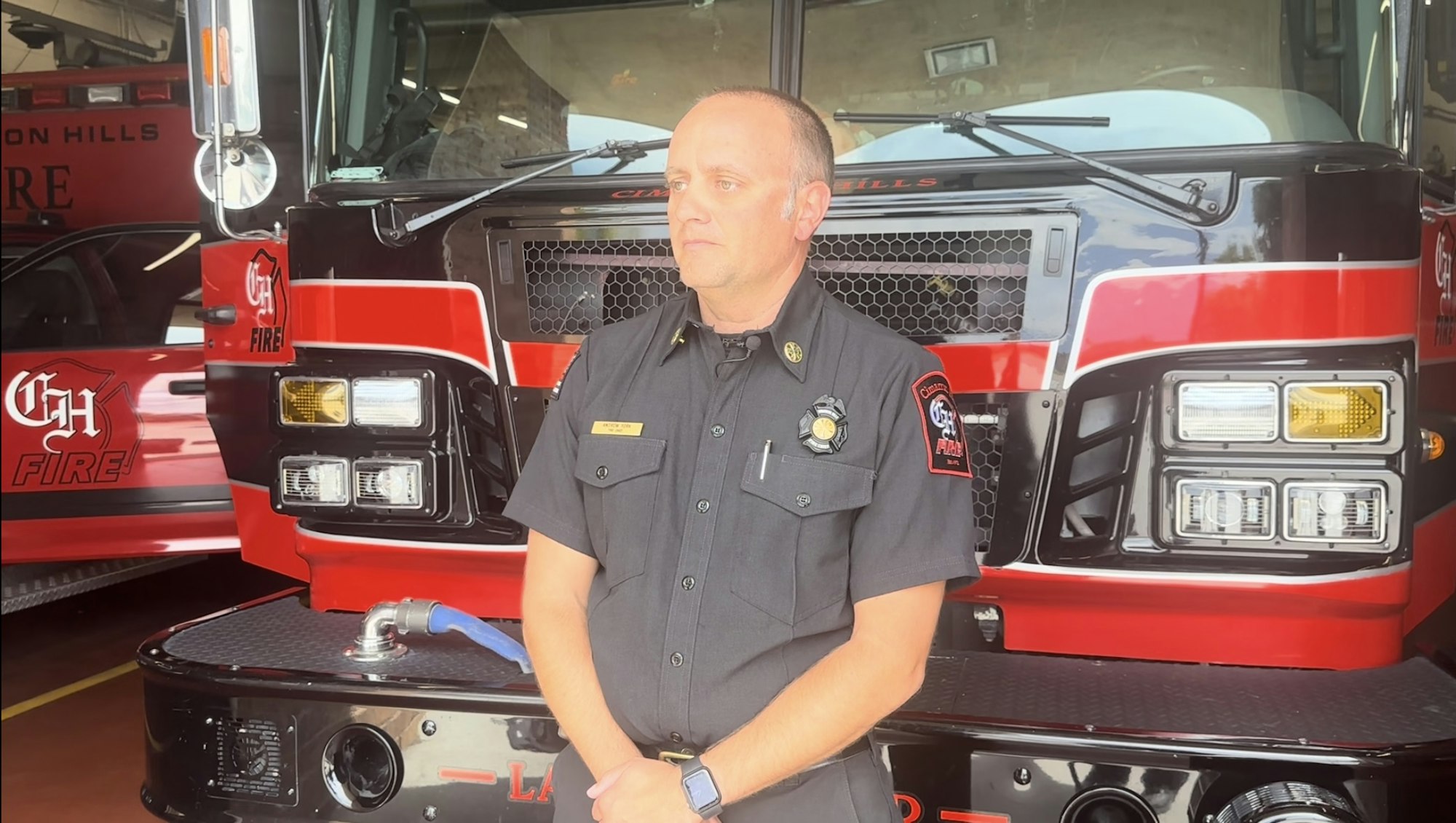 A firefighter in uniform standing in front of a fire truck.