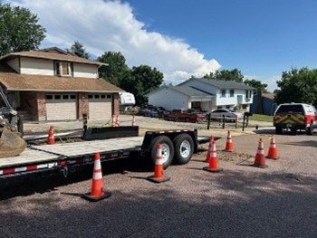 A trailer with traffic cones in front of suburban houses on a sunny day.