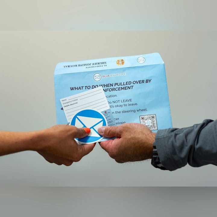 Two people holding a blue envelope with instructions for what to do when pulled over by law enforcement.