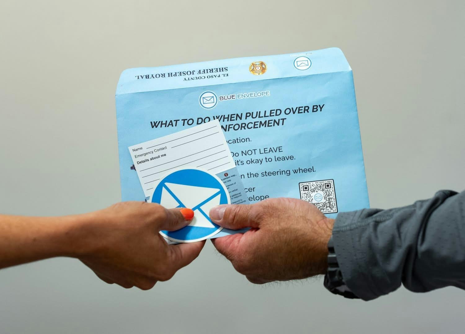 Two people holding a blue envelope with instructions for what to do when pulled over by law enforcement.