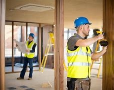 Construction workers in hard hats and safety vests using tools on a worksite.